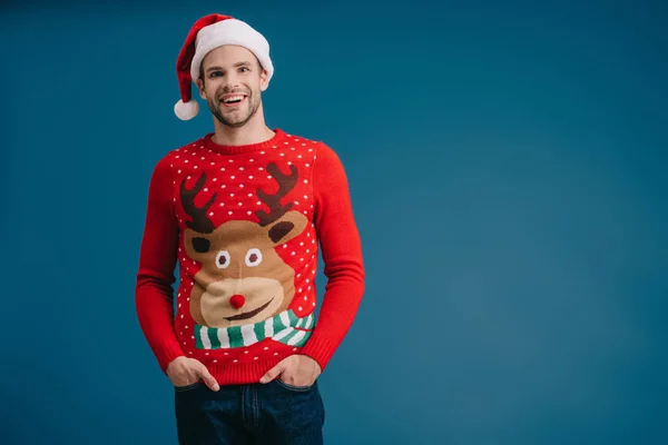 Lächelnder Mann posiert mit Weihnachtsmütze und Weihnachtspullover isoliert auf blauem Grund — Stockfoto