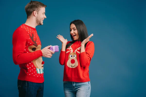 Man presenting christmas gift box to surprised woman isolated on blue — Stock Photo