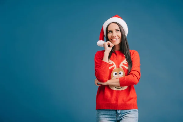 Улыбающаяся женщина, позирующая в шляпе Санты и рождественском свитере, изолированном на голубом — стоковое фото