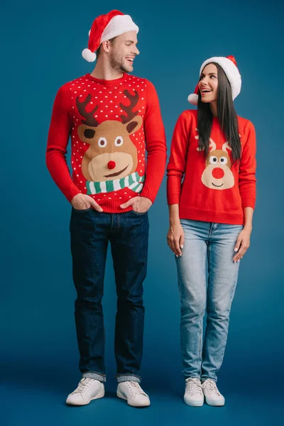 Beautiful couple posing in santa hats and sweaters on blue — Stock Photo