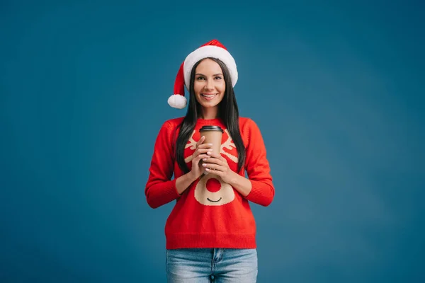Belle femme au chapeau de Père Noël et pull de Noël tenant café à emporter, isolée sur bleu — Photo de stock
