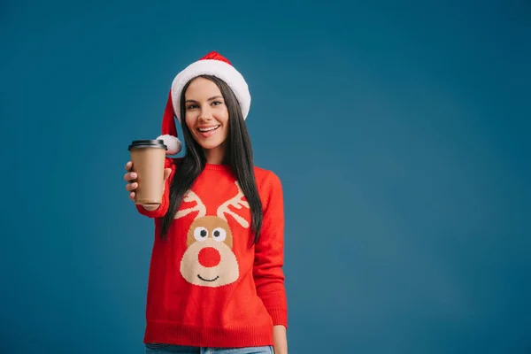 Весела жінка в капелюсі Санта тримає каву, щоб піти, ізольована на синьому — стокове фото