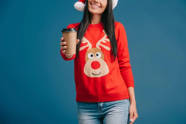 Abgeschnittene Ansicht eines lächelnden Mädchens mit Weihnachtsmütze und Weihnachtspullover mit Kaffee to go, isoliert auf blau — Stockfoto