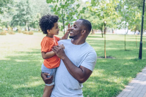 Alegre africano americano holding adorable hijo tocando su nariz - foto de stock