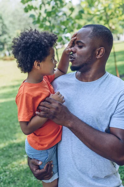 Cute african american boy touching nose of father while sitting on his arms — Stock Photo