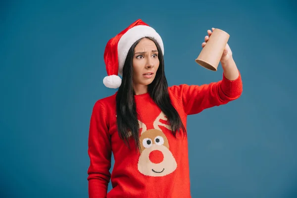 Donna sconvolta in cappello di Babbo Natale in possesso di tazza vuota di caffè, isolato su blu — Foto stock