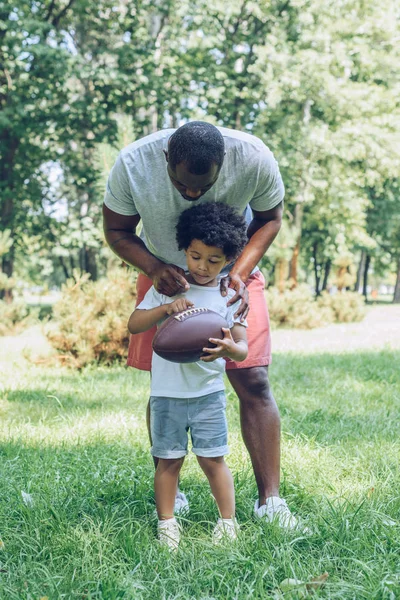 Young african american man hugging son holding rugby ball in park — Stock Photo