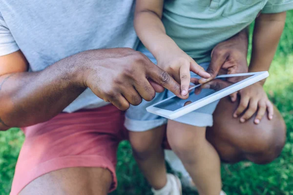 Partial view of african american father and son using digital tablet wit son in park — Stock Photo
