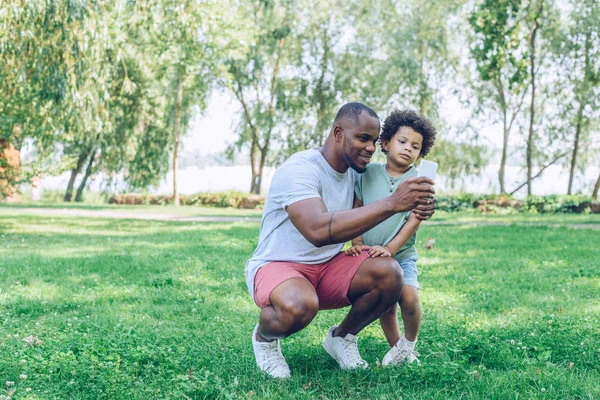 Jovem afro-americano pai tomando selfie com adorável filho no parque — Fotografia de Stock