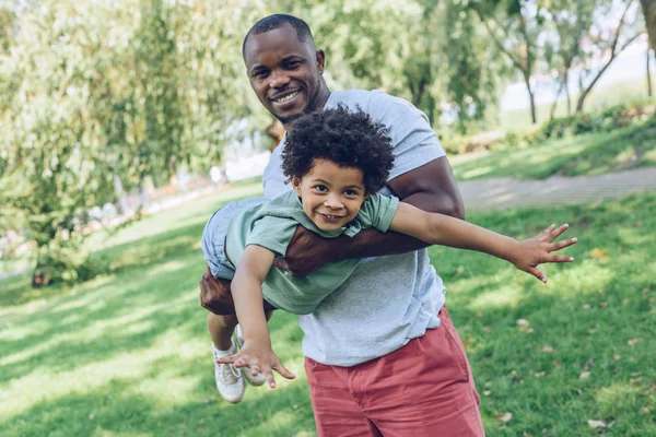 Молодий афроамериканський чоловік тримає чарівного сина, розважаючись у парку — стокове фото