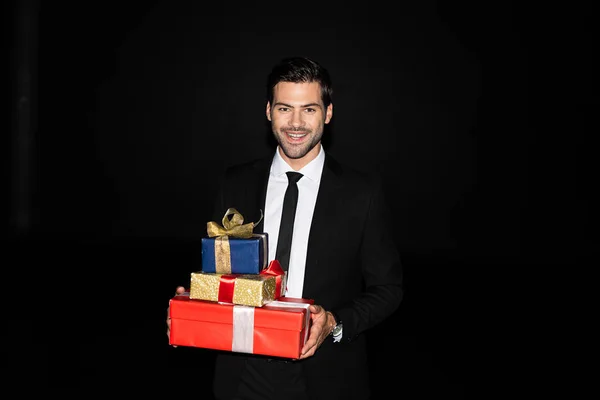 Hombre alegre elegante sosteniendo regalos, aislado en negro - foto de stock