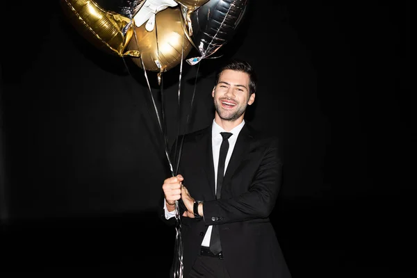 Sonriente hombre sosteniendo globos dorados para cumpleaños, aislado en negro - foto de stock