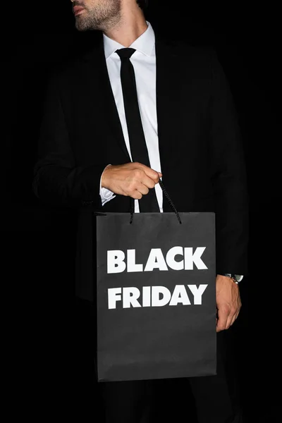 Vista recortada del hombre sosteniendo bolsa de compras con signo de viernes negro, aislado en negro - foto de stock