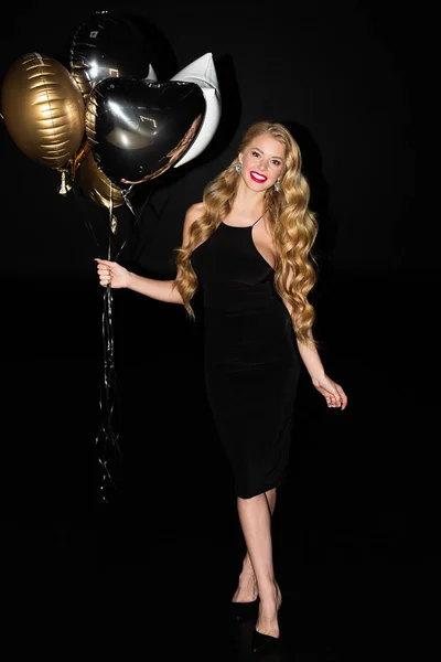 Belle fille à la mode tenant des ballons dorés isolés sur noir — Photo de stock