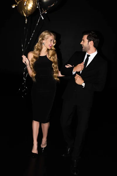 Hermosa pareja alegre con globos de oro en la fiesta aislado en negro - foto de stock