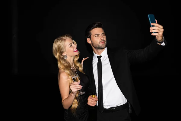 Beautiful couple taking selfie on smartphone with glasses on champagne isolated on black — Stock Photo