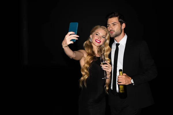 Heureux couple prendre selfie sur smartphone avec des lunettes sur champagne isolé sur noir — Photo de stock