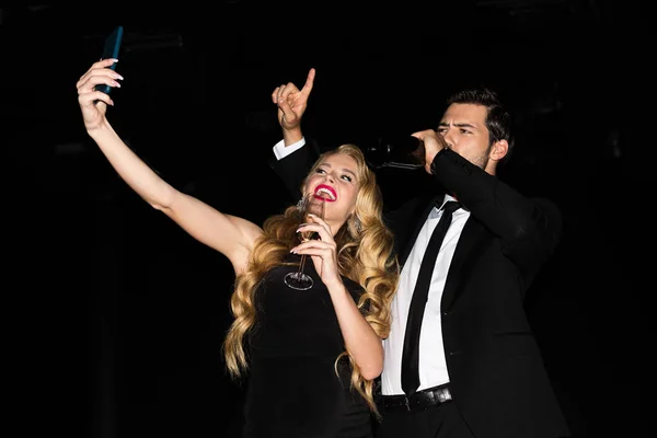 Красивая девушка и парень делает селфи на смартфоне с очками на шампанском изолированы на черном — стоковое фото