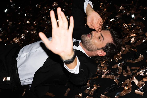 Sorrindo homem deitado no chão com confete dourado para férias — Fotografia de Stock