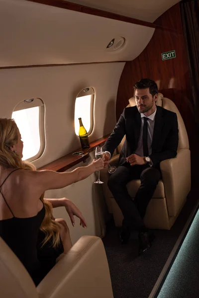 Couple à la mode cliquetis avec des verres de champagne tout en voyageant en avion — Photo de stock