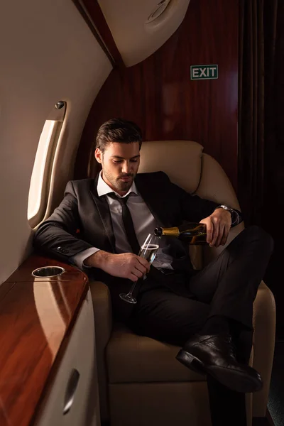 Handsome man pouring champagne into glass in plane — Stock Photo