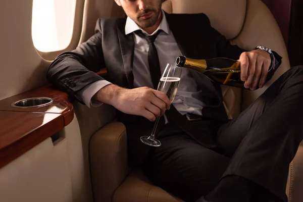 Cropped view of man pouring champagne into glass in plane — Stock Photo
