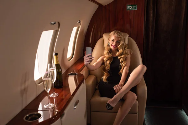 Sexy attrayant femme prendre selfie sur smartphone avec champagne dans l'avion — Photo de stock
