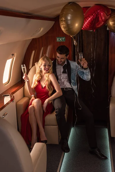 Hermosa pareja joven con champán sentado en el avión - foto de stock