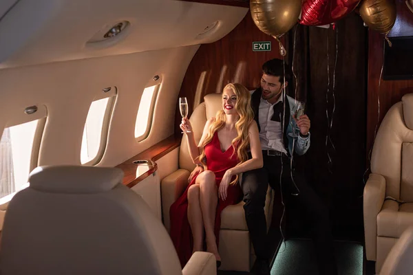 Young sexy couple with champagne sitting in airplane with balloons — Stock Photo
