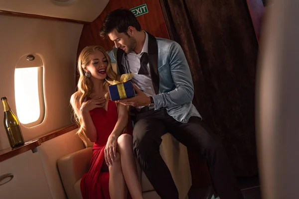 Homem apresentando caixa de presente para mulher loira feliz no avião — Fotografia de Stock