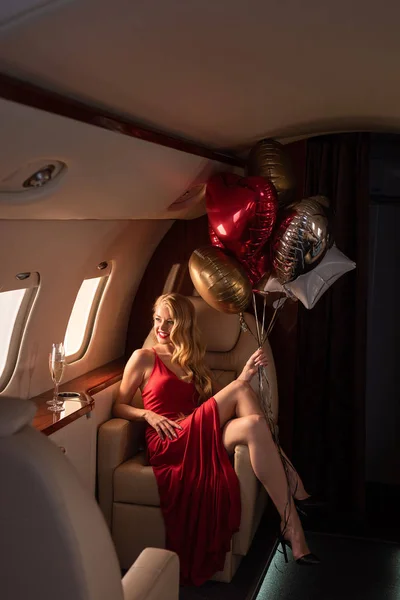 Sexy attractive woman with champagne and balloons sitting in plane — Stock Photo