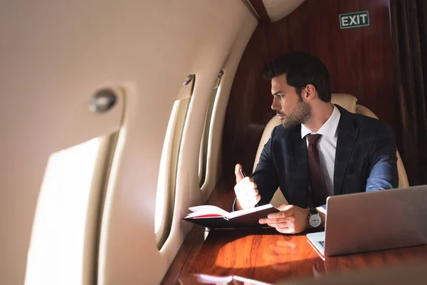 Joven hombre de negocios que trabaja con portátil y portátil en avión durante su viaje de negocios - foto de stock