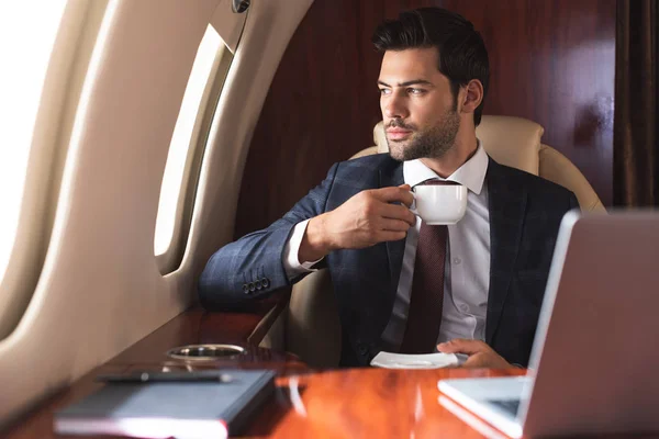 Бизнесмен в костюме пьет кофе в самолете во время деловой поездки — стоковое фото