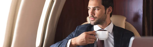 Уверенный в себе бизнесмен в костюме пьет кофе в самолете во время деловой поездки — стоковое фото