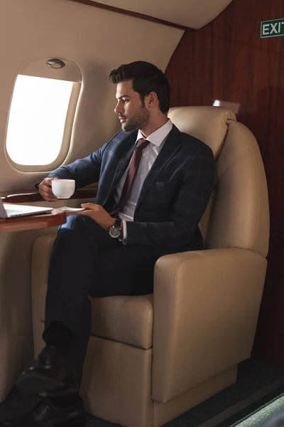Hombre de negocios serio en traje de beber café en avión durante su viaje de negocios - foto de stock