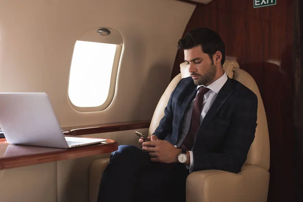 Бизнесмен работает на смартфоне и ноутбуке в самолете во время деловой поездки — стоковое фото