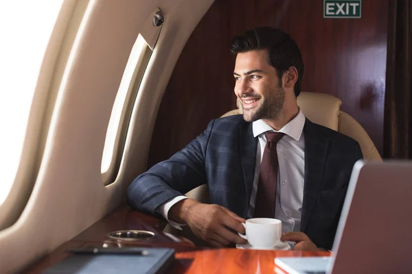 Uomo d'affari sorridente che tiene la tazza di caffè in aereo durante il viaggio d'affari — Foto stock