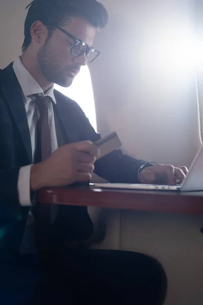 Красивый бизнесмен с кредитной картой и ноутбуком в самолете — стоковое фото