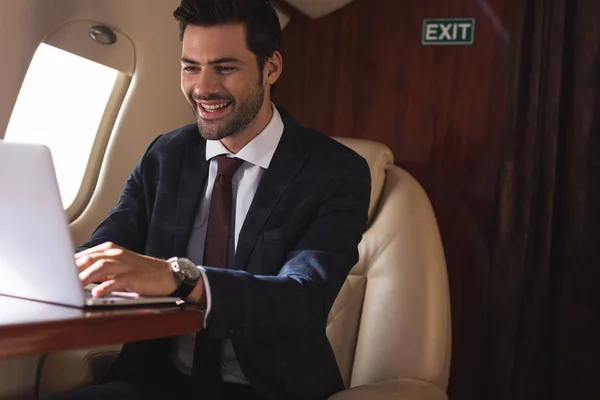 Homme d'affaires joyeux travaillant avec ordinateur portable dans l'avion pendant le voyage d'affaires — Photo de stock