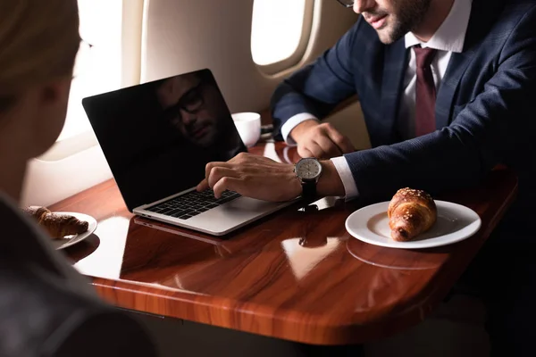 Cropped view of businesspeople working with laptop in airplane — Stock Photo