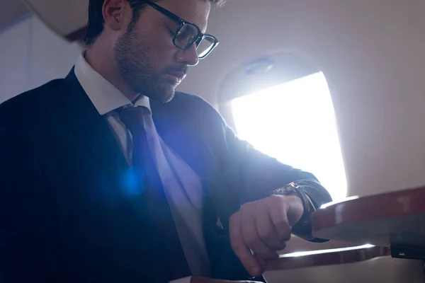 Homme d'affaires sérieux regardant regarder pendant qu'il est assis dans un avion — Photo de stock