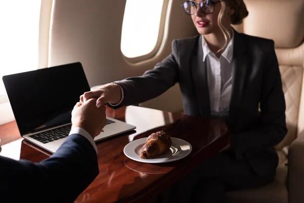 Business colleagues in formal wear shaking hands in plane with laptop — Stock Photo