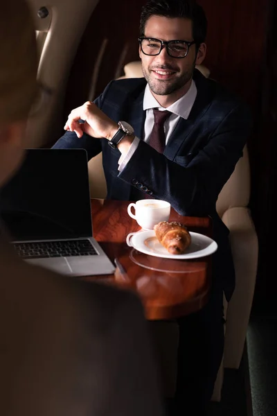 Professional businesspeople working with laptop, coffee and croissant sitting in plane — Stock Photo