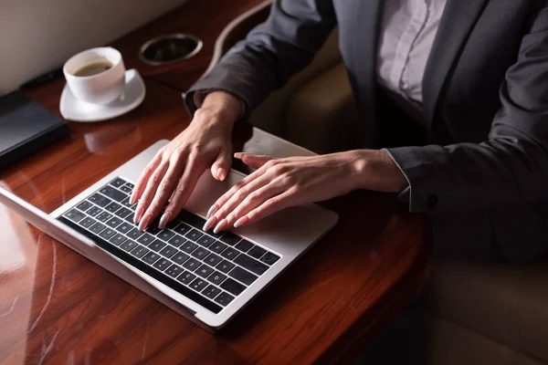 Cropped view of businesswoman working on laptop in plane during business trip — Stock Photo