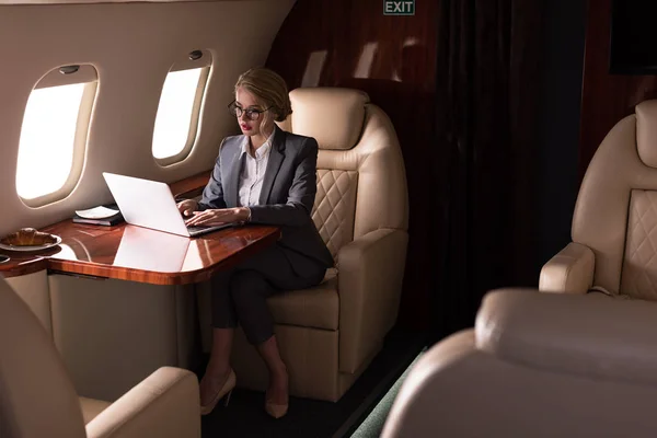 Confident businesswoman working on laptop in plane during business trip — Stock Photo