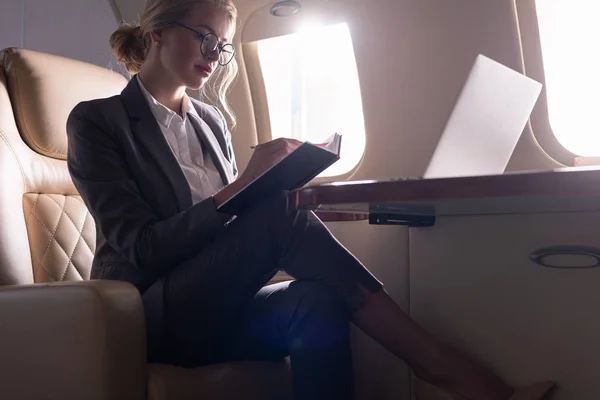 Привлекательная деловая женщина, работающая с документами и ноутбуком в самолете во время деловой поездки — стоковое фото