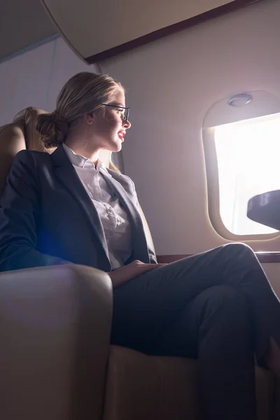 Mujer de negocios en gafas mirando a la ventana en avión durante su viaje de negocios - foto de stock