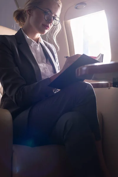 Mujer de negocios rubia trabajando con documentos en avión durante su viaje de negocios - foto de stock