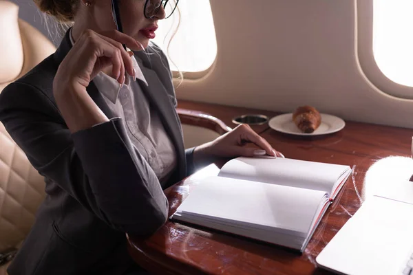 Cropped view of businesswoman working with documents in plane during business trip — Stock Photo