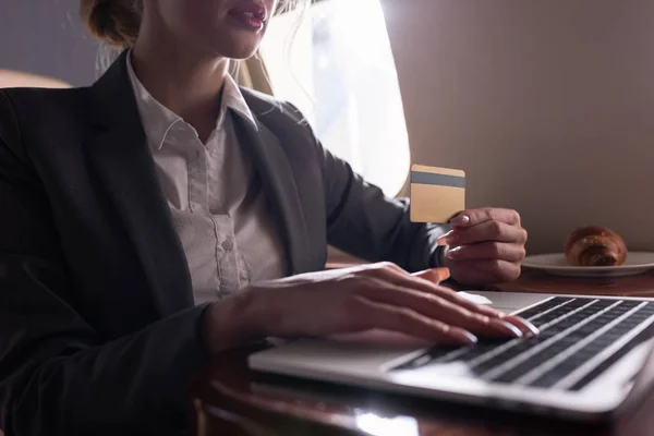 Cropped view of businesswoman working credit card and laptop in plane during business trip — Stock Photo